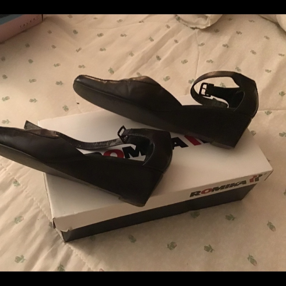 Black leather wedge shoes, strap fastens around ankle.